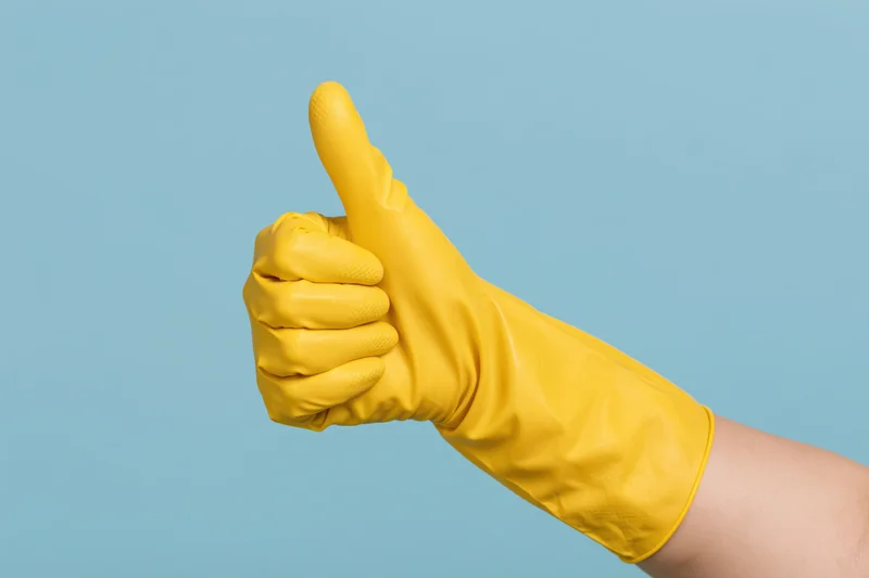 Hand in yellow rubber cleaning glove giving thumbs up against blue background