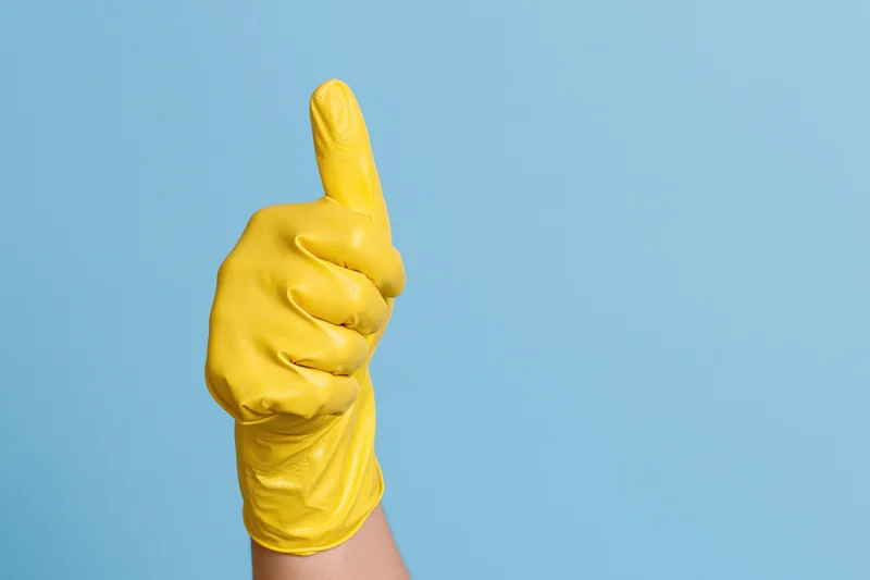 Hand in yellow rubber cleaning glove giving thumbs up against blue background