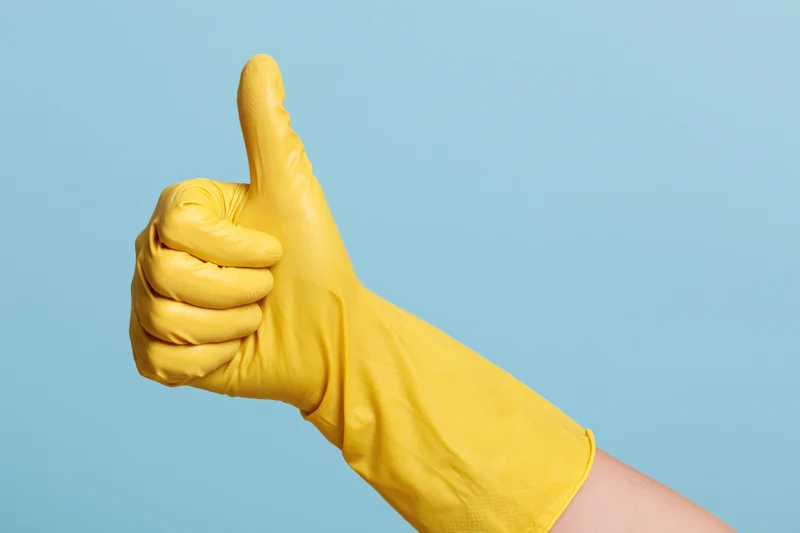 Hand in yellow rubber cleaning glove giving thumbs up against blue background