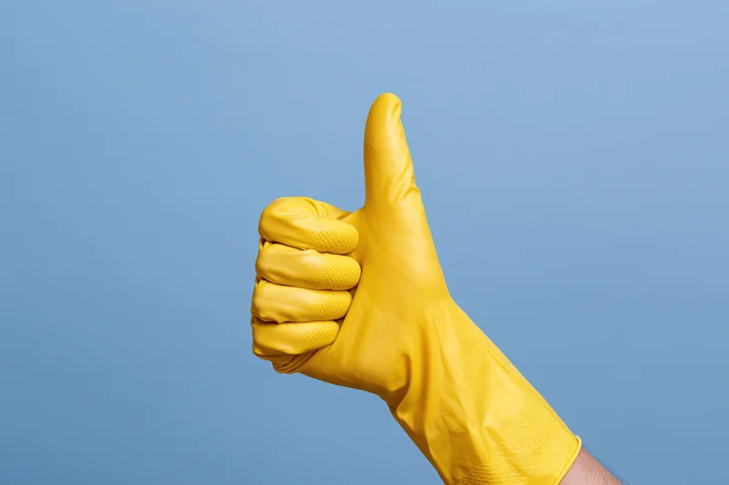Hand in yellow rubber cleaning glove giving thumbs up against blue background