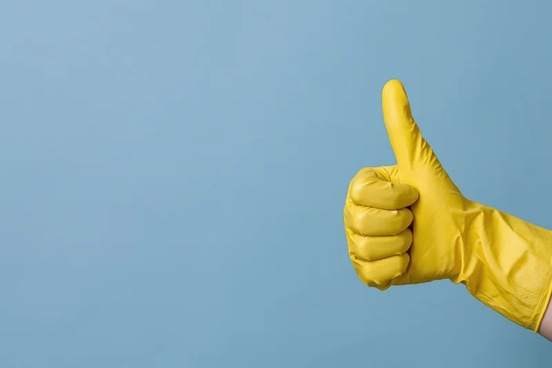 Hand in yellow rubber cleaning glove giving thumbs up against blue background