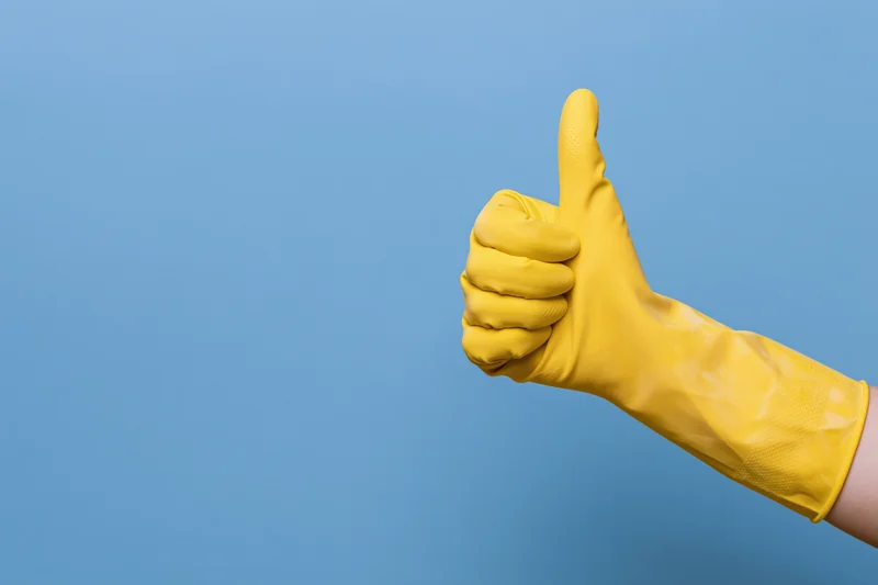 Hand in yellow rubber cleaning glove giving thumbs up against blue background