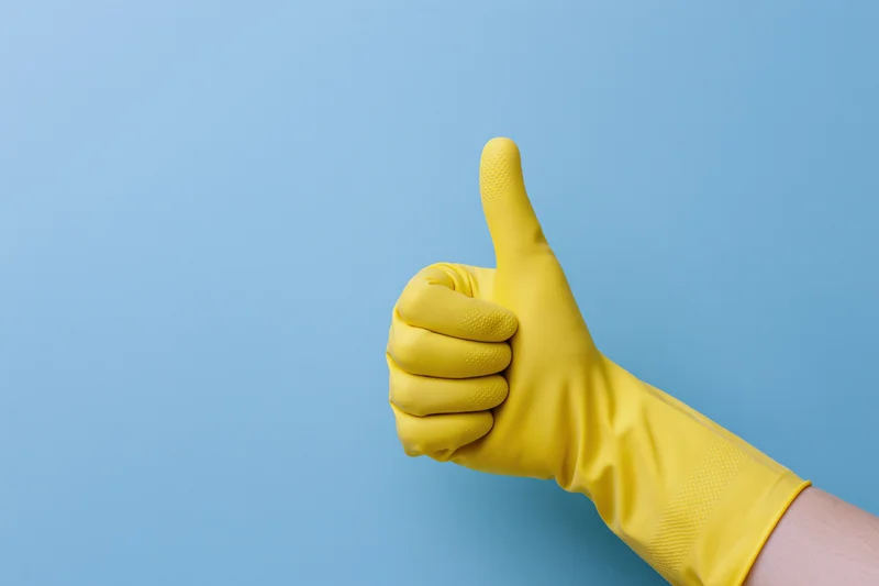 Hand in yellow rubber cleaning glove giving thumbs up against blue background