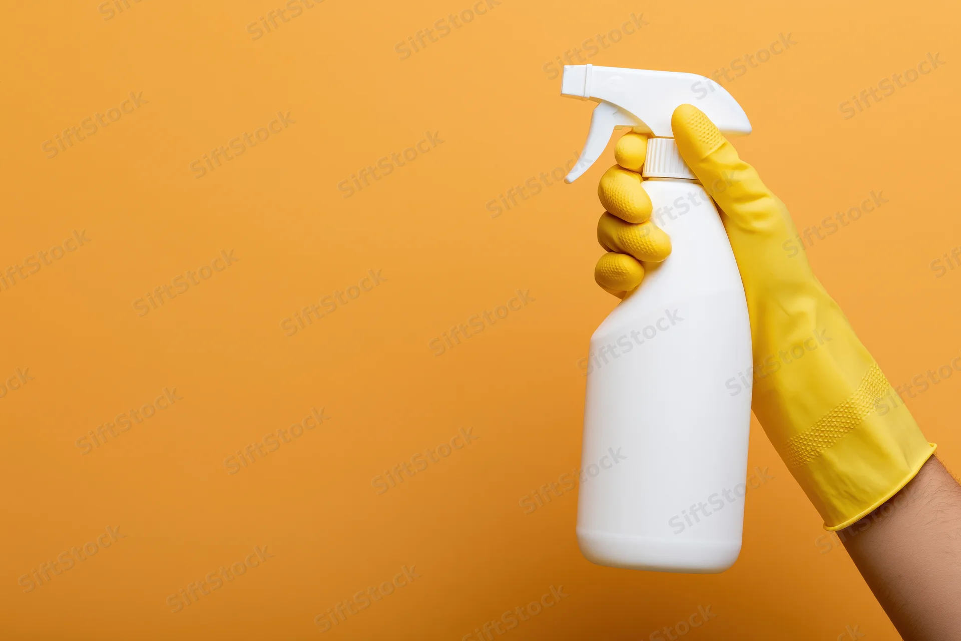Hand in yellow rubber glove holding white spray bottle against orange background