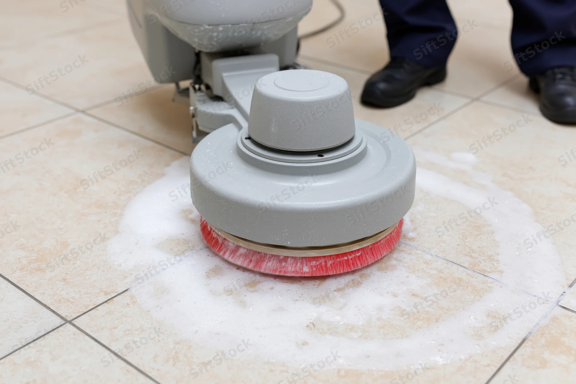 Janitor operating rotary floor scrubbing machine on tiled floor