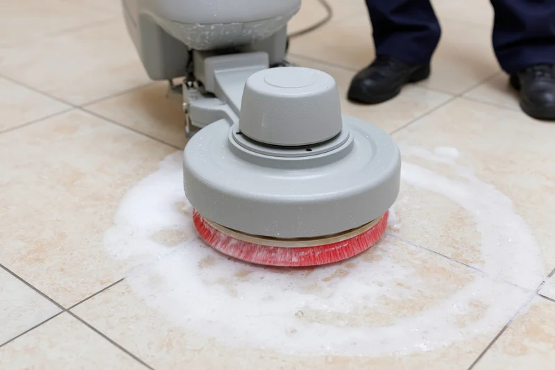 Janitor operating rotary floor scrubbing machine on tiled floor