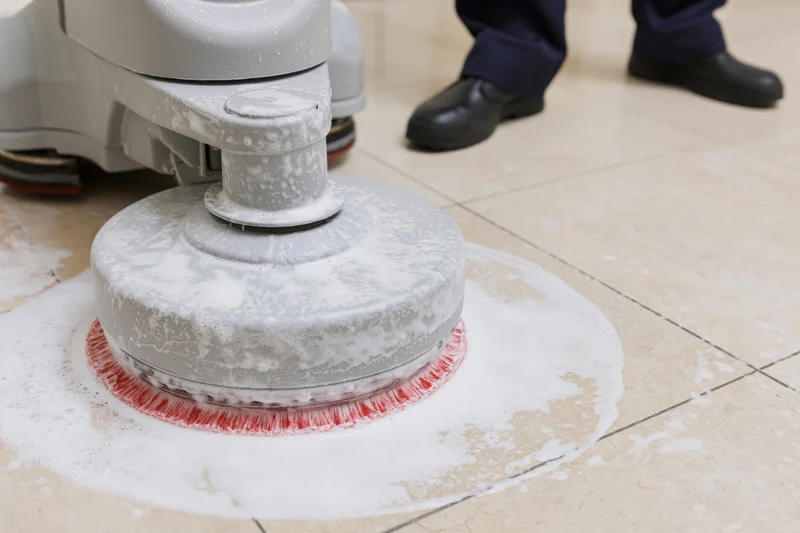 Janitor operating a gray rotary floor scrubber on tile floor