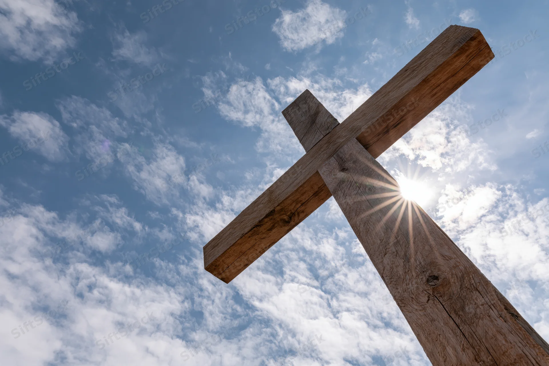 Wooden christian cross against blue sky with sunburst and scattered clouds