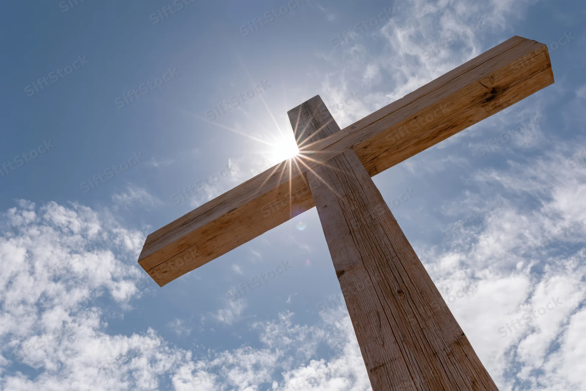 Wooden christian cross against blue sky with sun shining through, low angle view