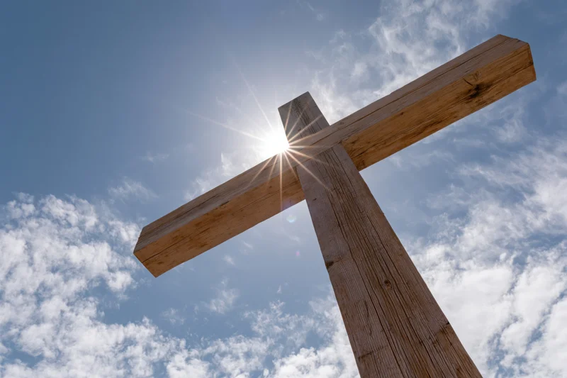 Wooden christian cross against blue sky with sun shining through, low angle view
