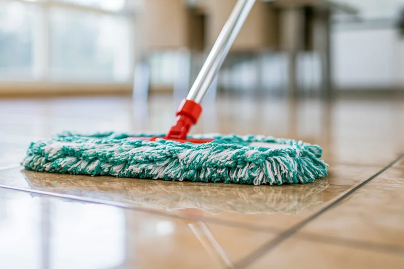 Microfiber mop head resting on polished tile floor with chrome handle and red connector
