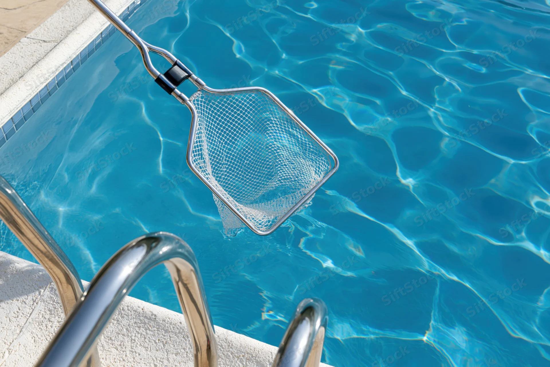 Pool cleaning net skimmer dipping into clear blue swimming water near metal ladder steps