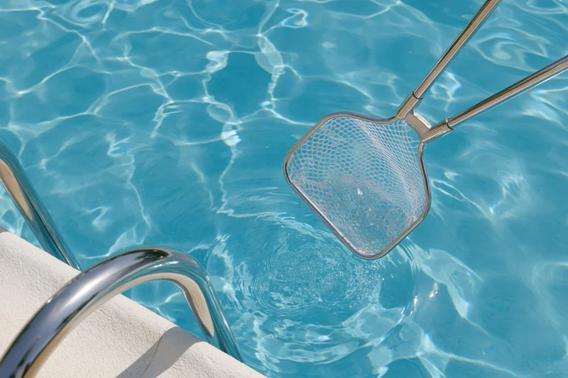 Pool skimmer net dipping into clear blue water near pool ladder