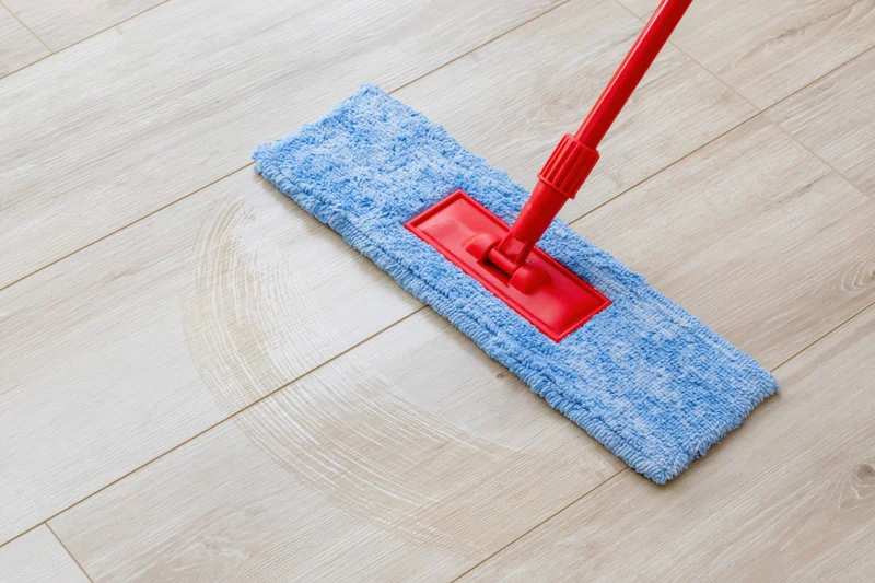 Red flat mop with blue microfiber pad cleaning light wood laminate floor