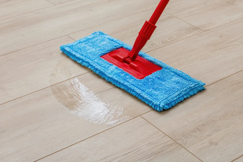 Red flat mop with blue microfiber pad cleaning light wood laminate floor