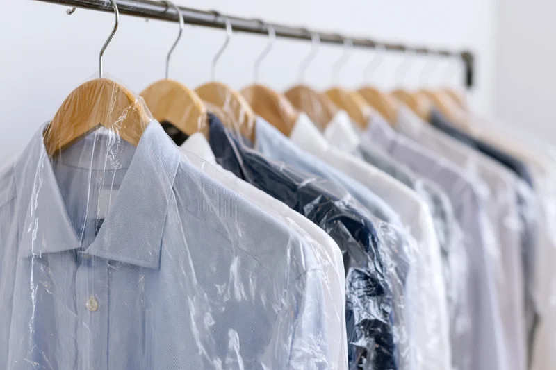 Row of freshly dry-cleaned shirts on wooden hangers in a closet