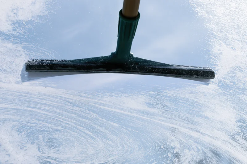 Rubber squeegee wiping soapy water from a glass window surface