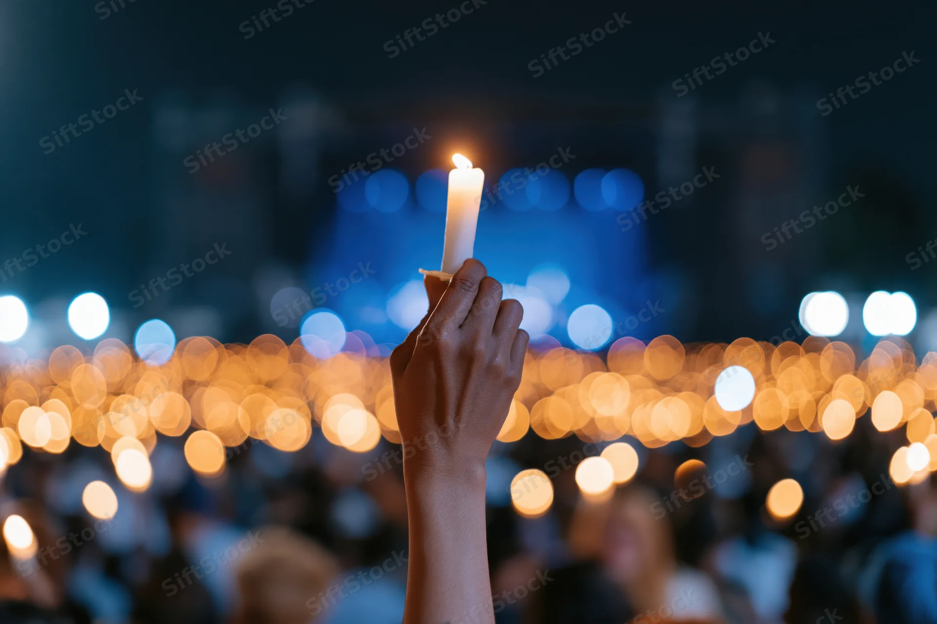 Hand holding lit candle raised high at night during outdoor vigil
