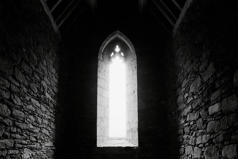 Tall gothic arch window glowing with light in stone church interior