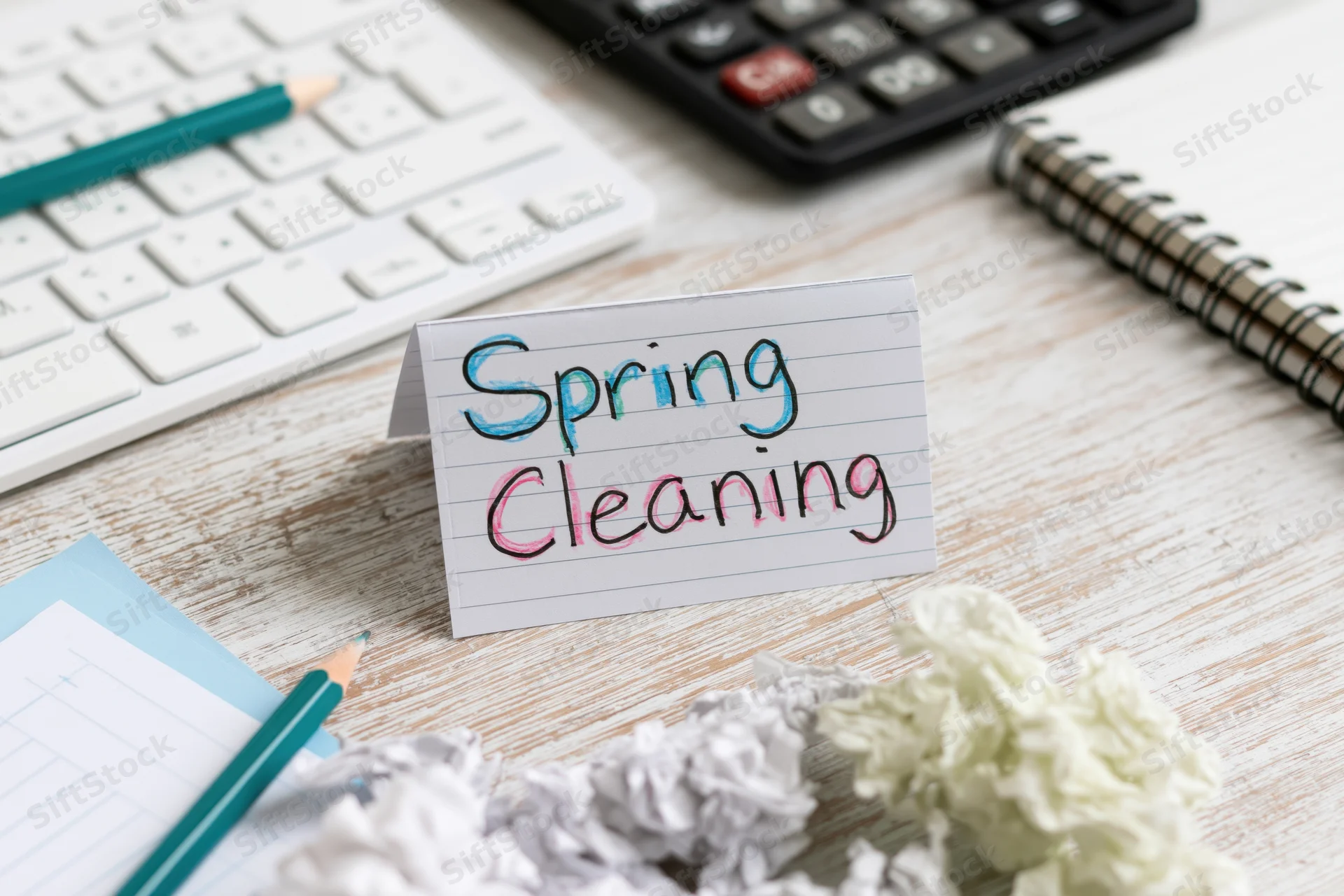 Handwritten spring cleaning note on a desk with office supplies and crumpled paper