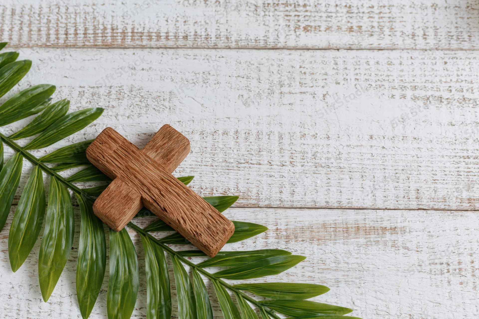 Wooden cross resting on green palm leaf on white rustic wood surface