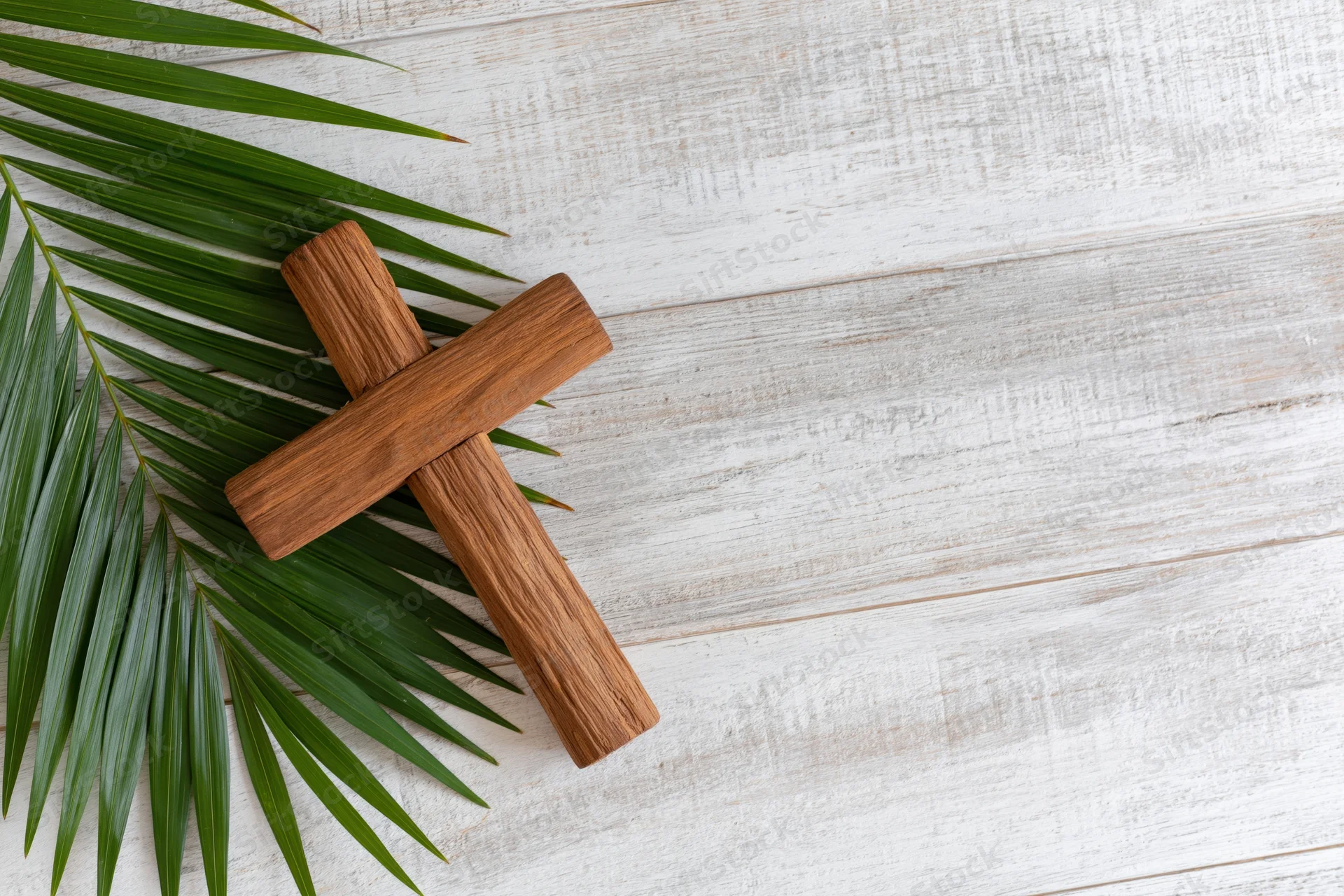 Wooden cross resting beside green palm leaf on white wooden surface