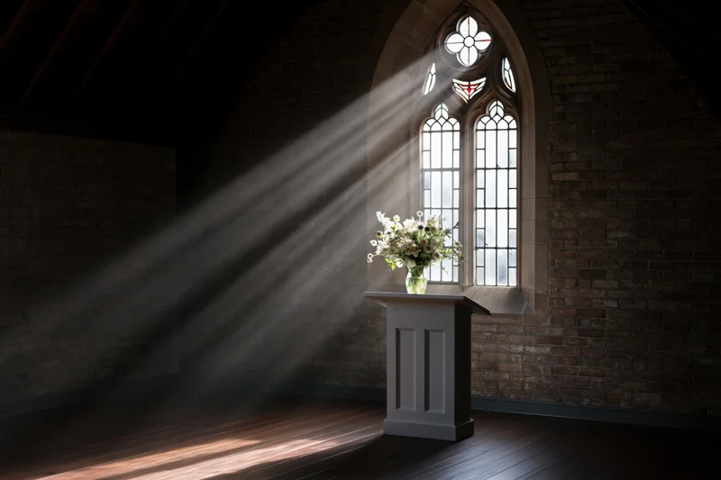 Sunlight streaming through a gothic window onto a white pulpit with flowers in a church interior