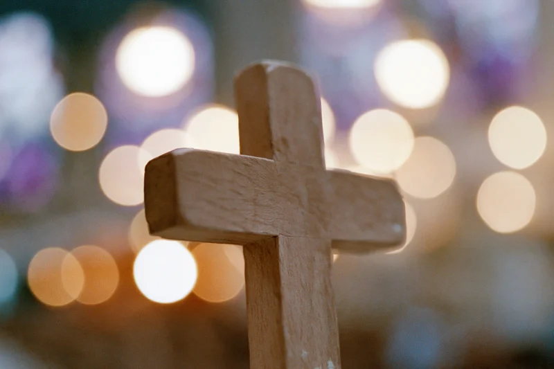 Wooden cross in closeup with blurred lights in background
