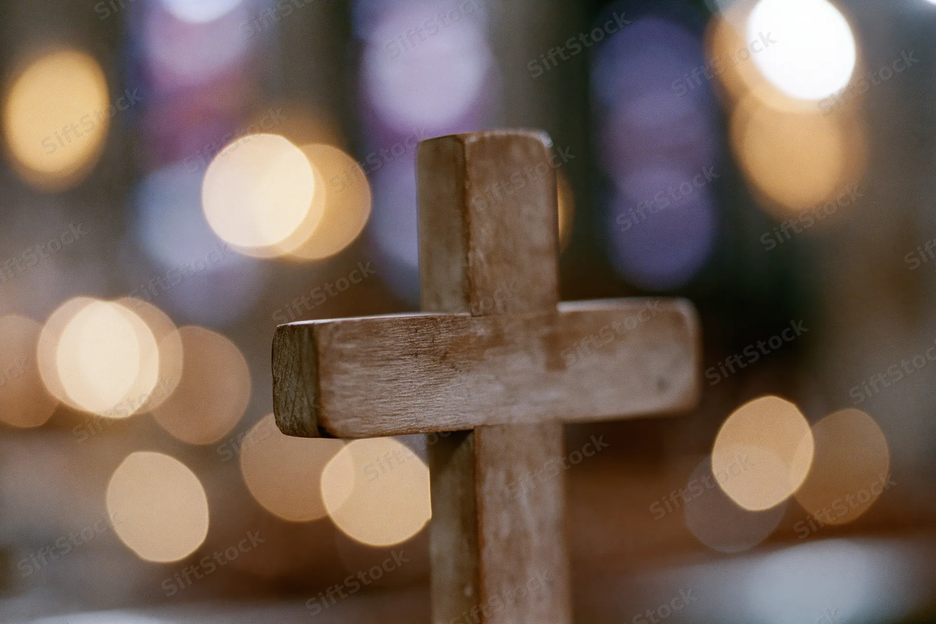 Small worn wooden cross standing upright in a softly lit church interior with blurred candlelight in the background