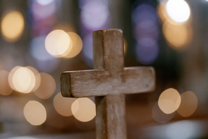 Small worn wooden cross standing upright in a softly lit church interior with blurred candlelight in the background