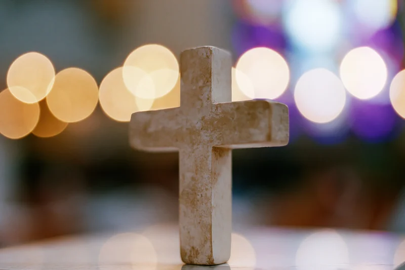 Small worn wooden cross standing upright with blurred lights behind it