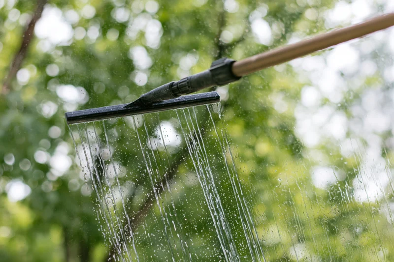 Squeegee on extension pole removing water from glass window outdoors