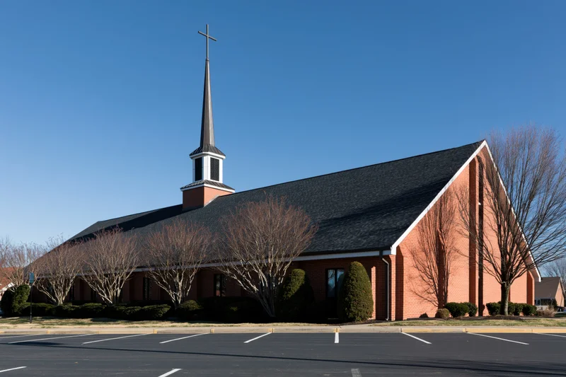 Brick church with central steeple and cross under clear blue sky in suburban setting