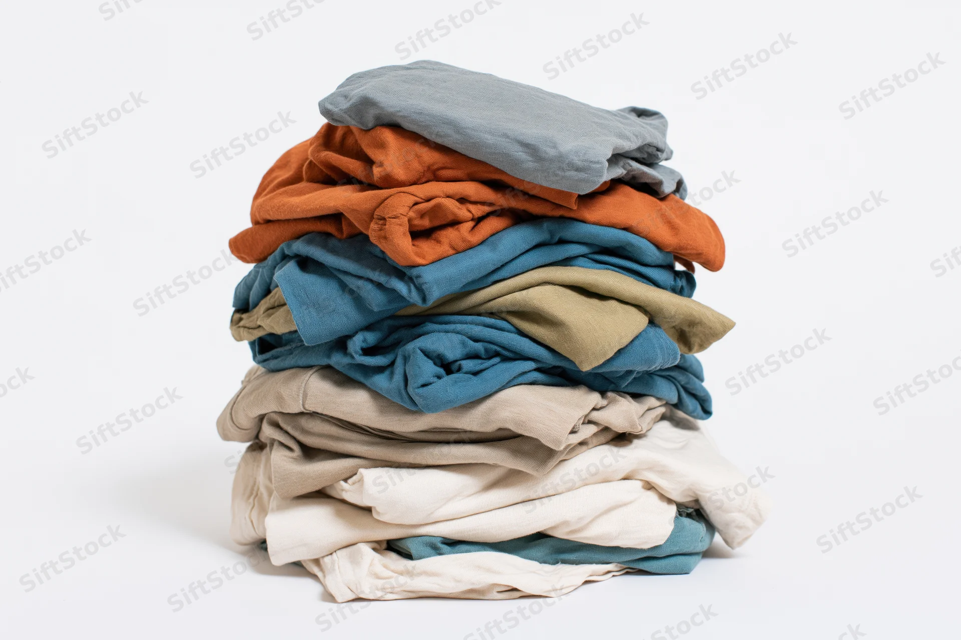 Tall messy pile of folded casual t-shirts stacked on white background