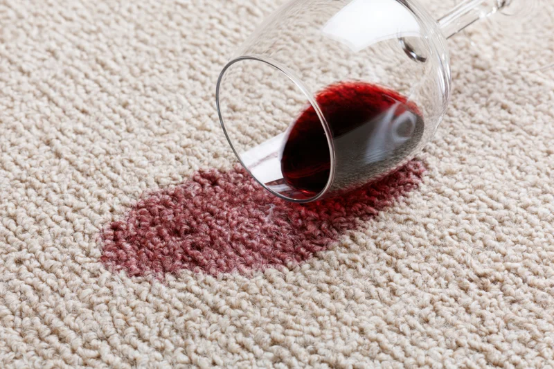 Tipped wine glass spilling red liquid onto beige carpet