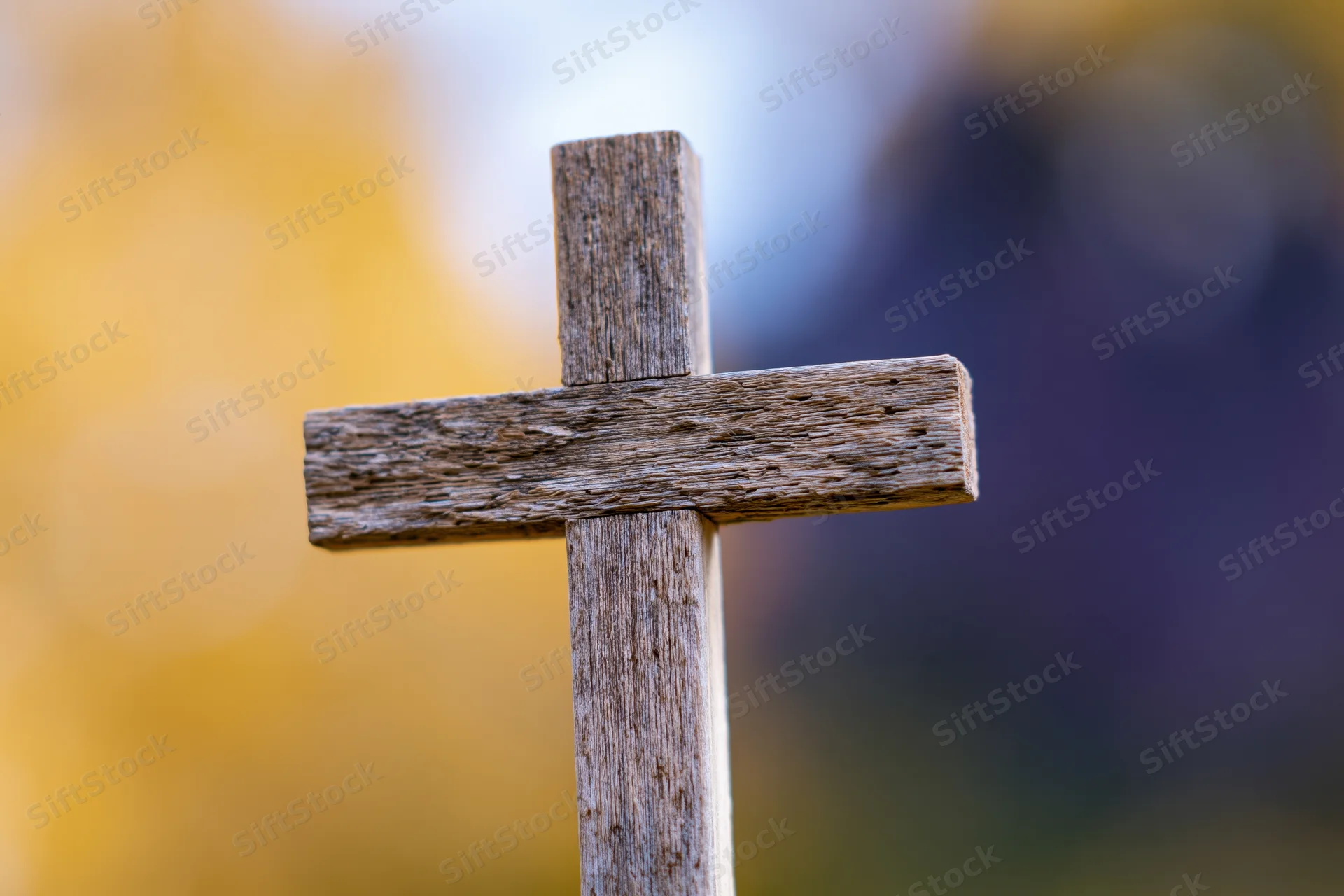Weathered wooden cross standing upright in a cemetery with blurred autumn foliage background