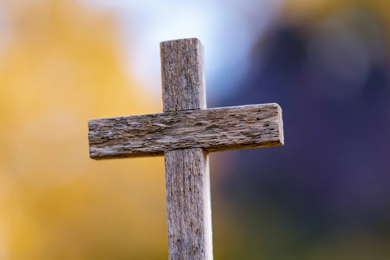 Weathered wooden cross standing upright in a cemetery with blurred autumn foliage background