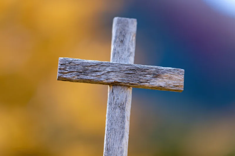 Weathered wooden cross standing upright in a blurred autumn landscape