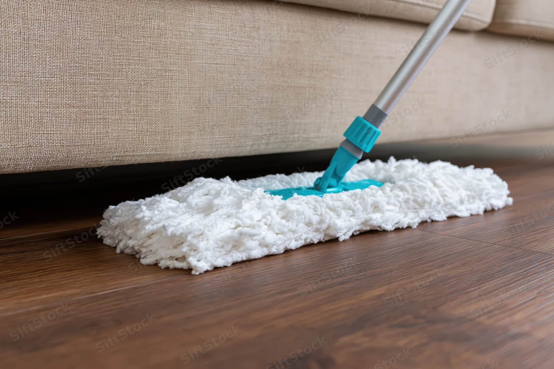 White microfiber mop cleaning hardwood floor near beige sofa
