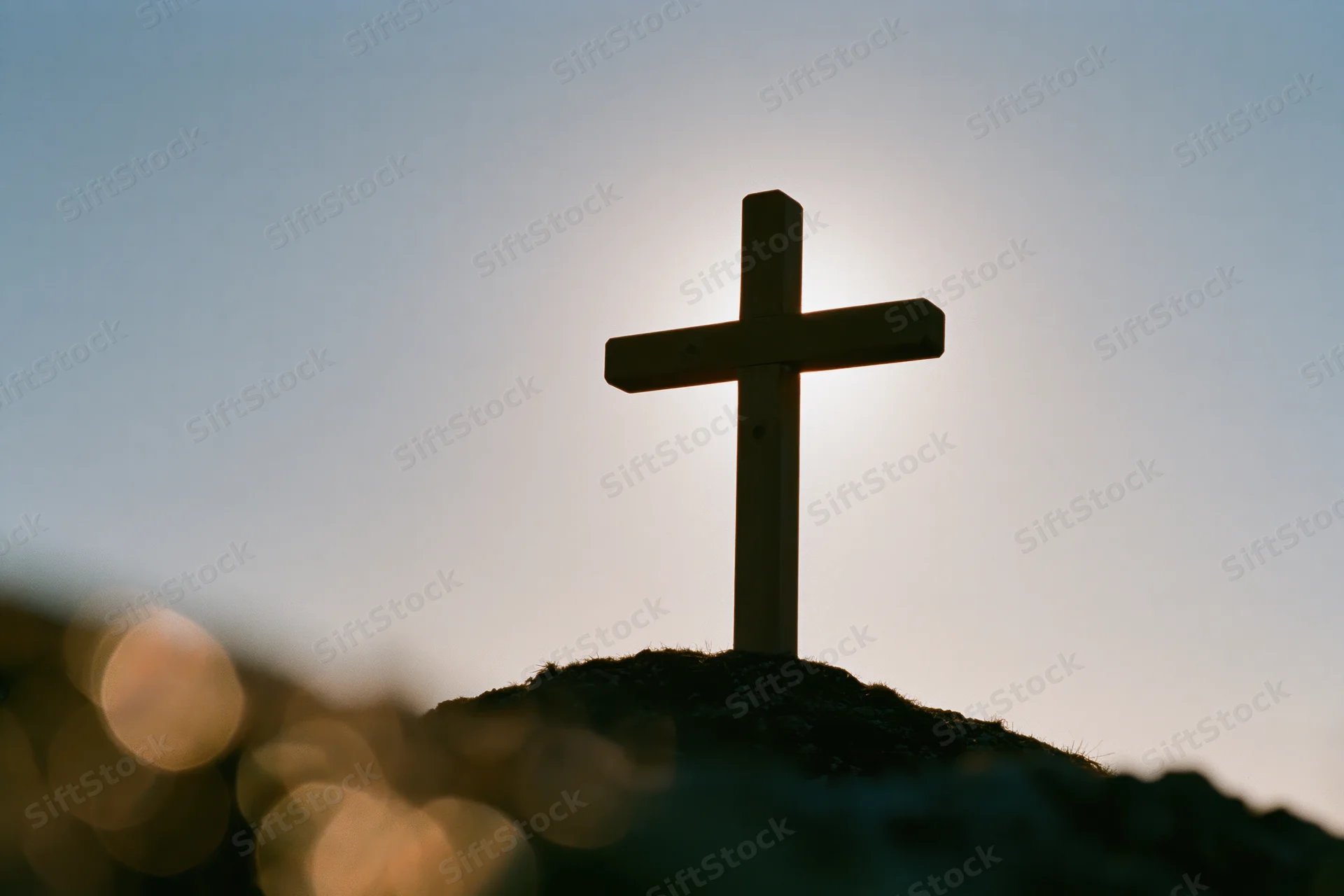 Wooden christian cross silhouetted on a small mound against twilight sky
