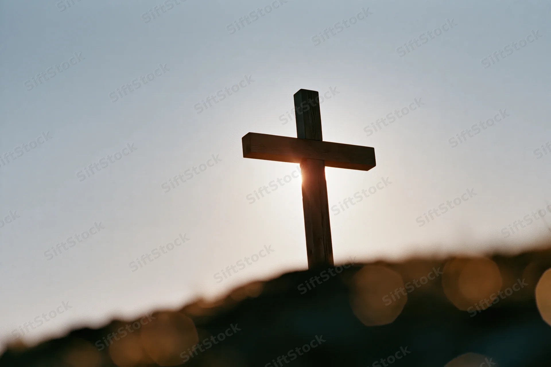 Wooden christian cross silhouetted against sunset sky on a small mound