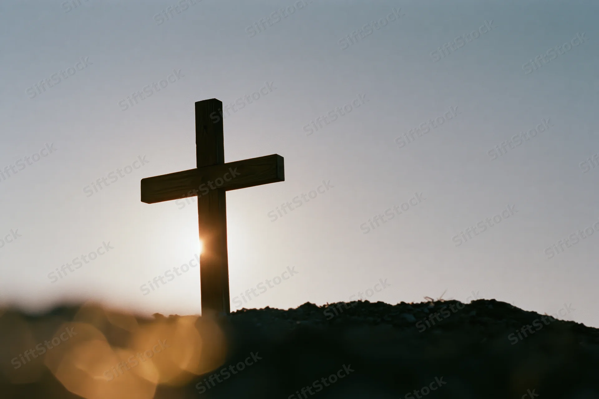 Wooden christian cross silhouetted against sunset sky on a small mound