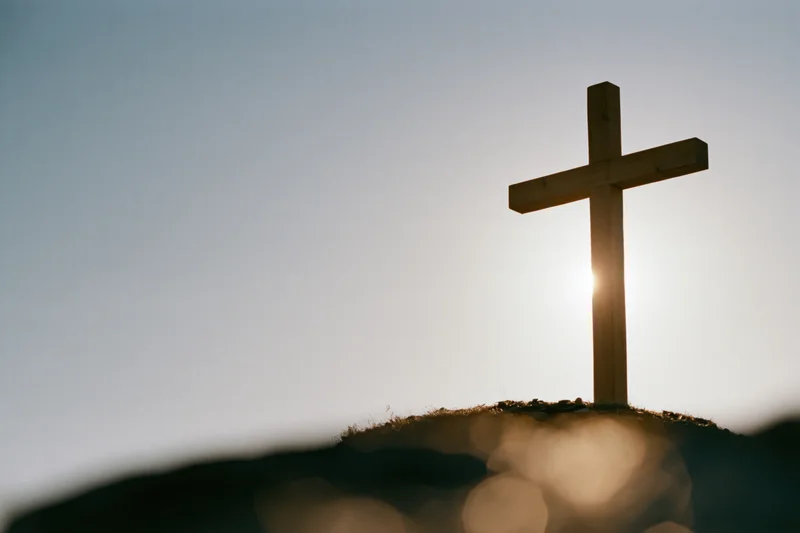 Wooden christian cross silhouetted on a mound at sunset