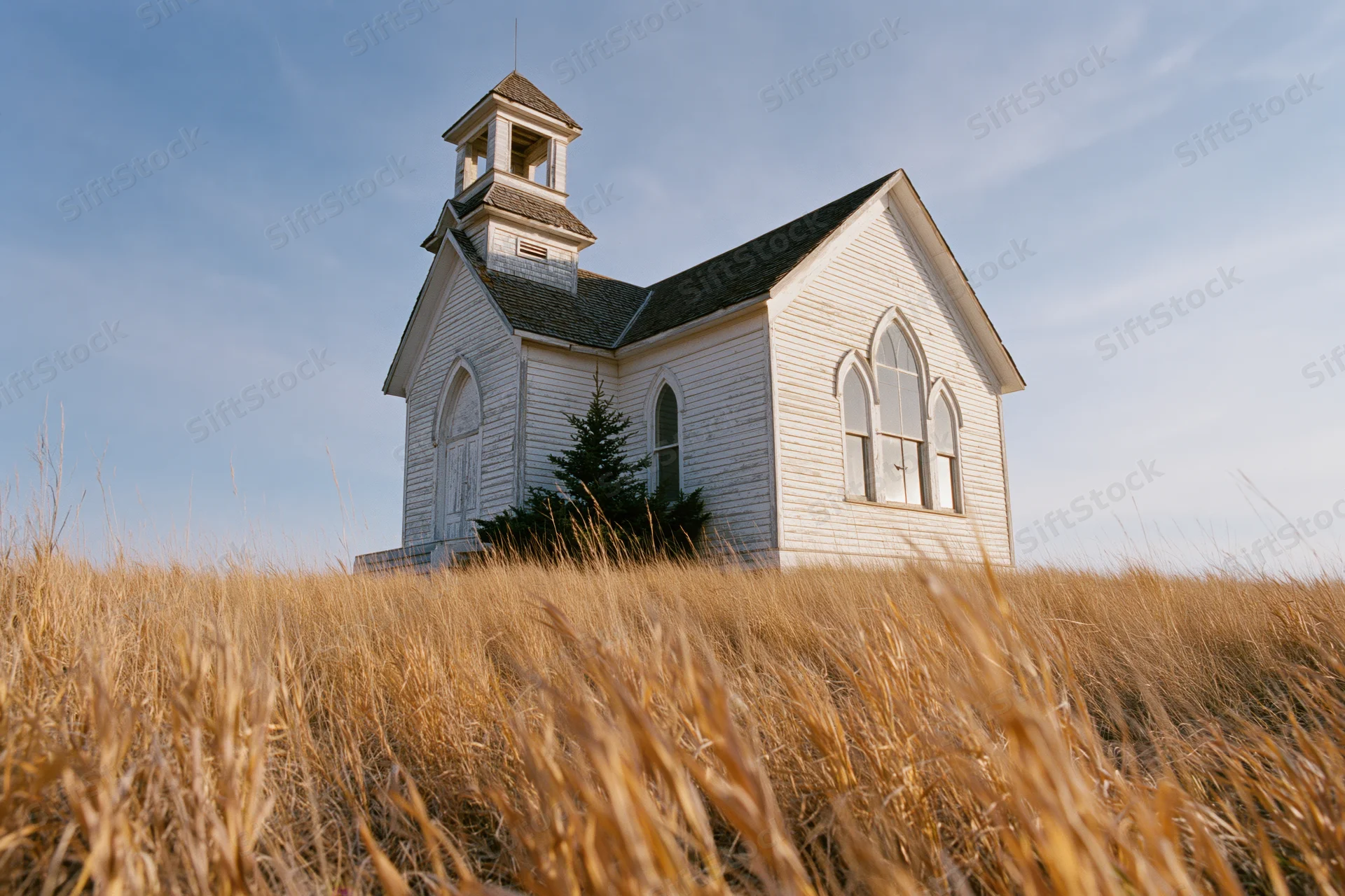 White clapboard church with small bell tower stands in golden grass field under blue sky