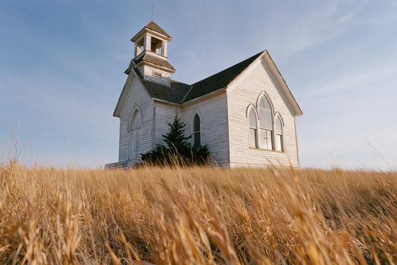 White clapboard church with small bell tower stands in golden grass field under blue sky