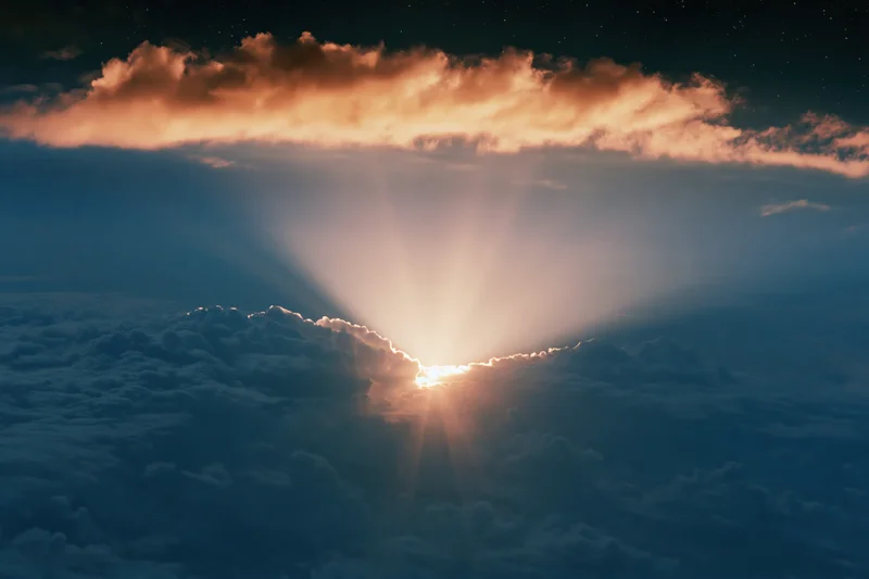 Sun emerging from clouds casting rays upward through layered cloud cover in aerial sky view