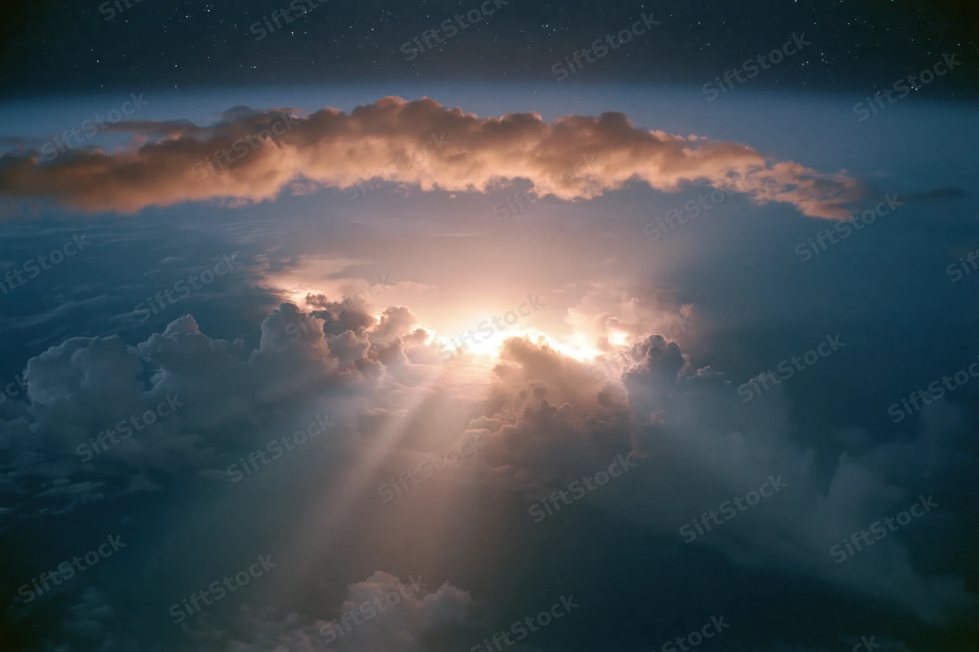 Aerial view through layered clouds toward sun rising above horizon