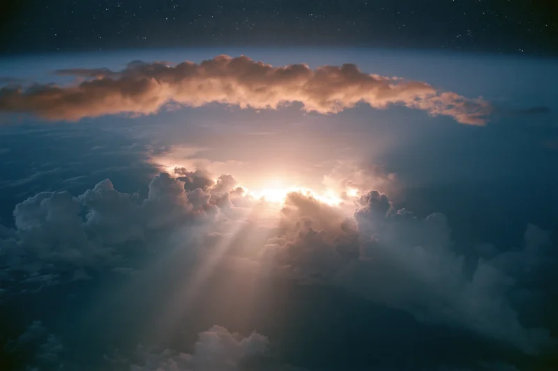 Aerial view through layered clouds toward sun rising above horizon
