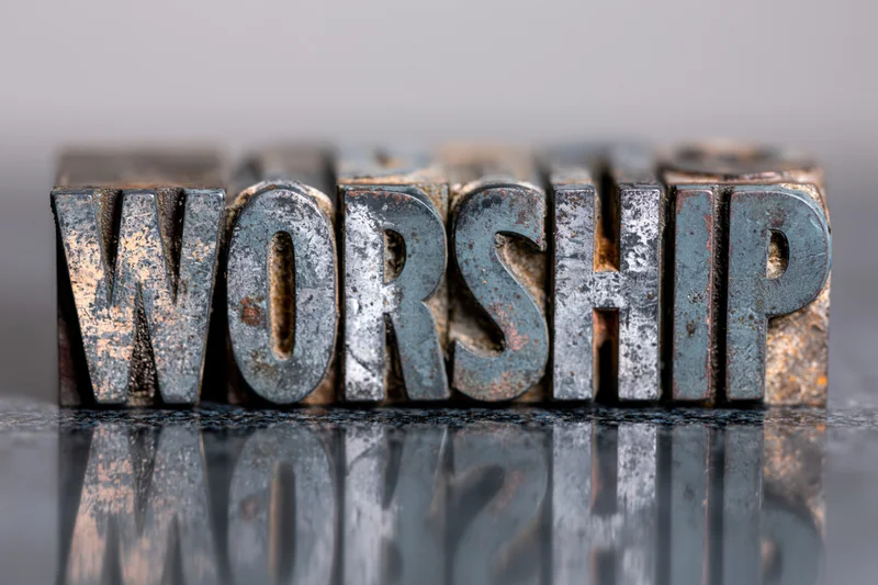 Antique metal letterpress blocks spelling worship arranged in a row on a reflective surface
