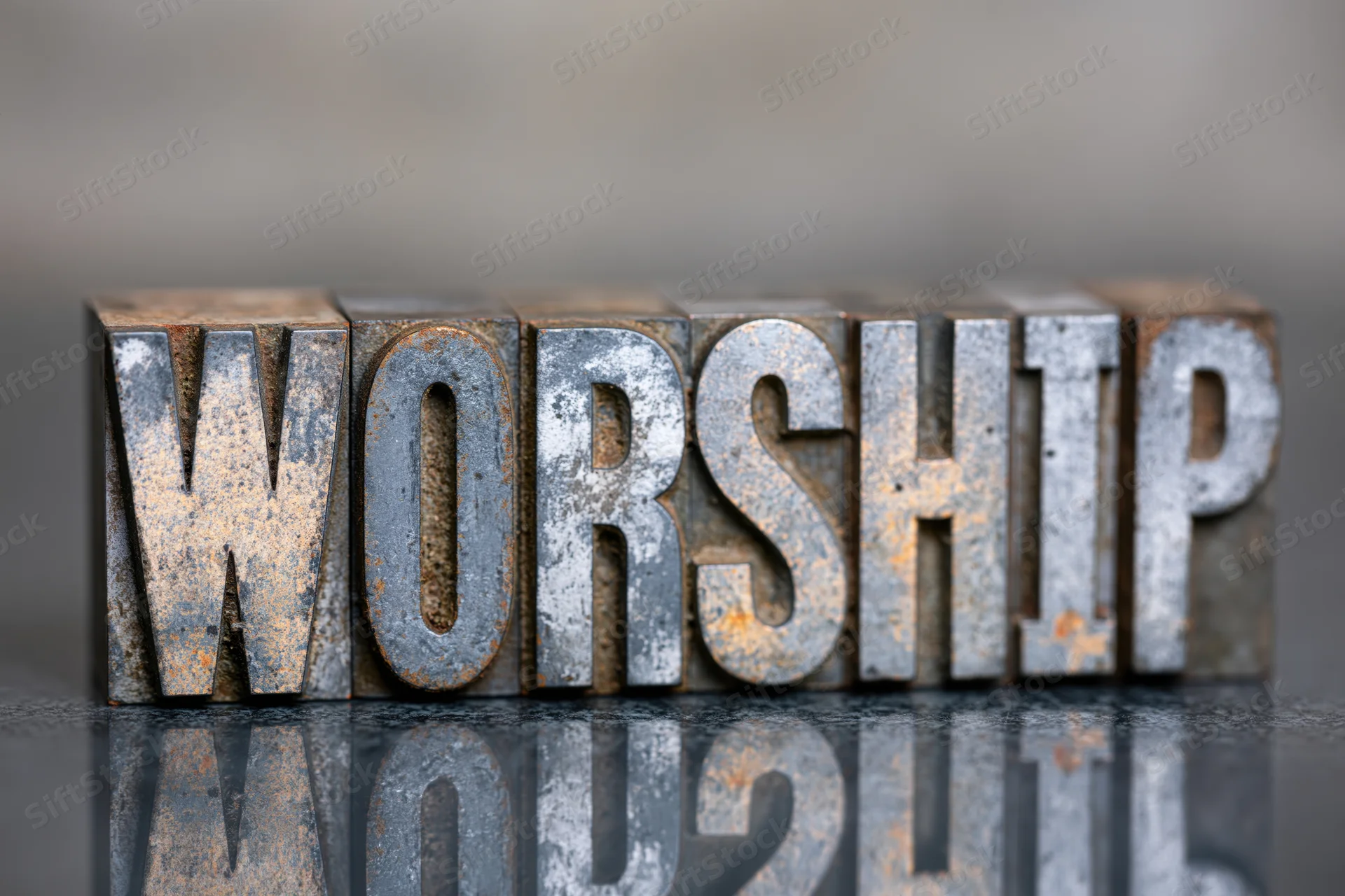 Antique metal letterpress blocks spelling worship arranged in a row on a reflective surface